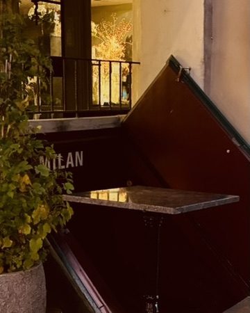 Eingang der Milan Bar mit Tisch und Pflanze